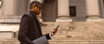 A man holding a laptop znd looking into phone.