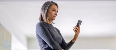 Person in a grey sweater holding a smartphone while standing indoors