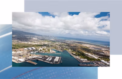 Aerial view of a coastal city with an industrial harbor and a dense urban skyline under a partly cloudy sky.