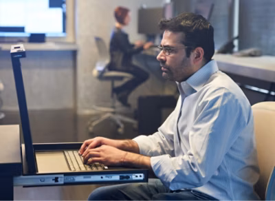 A man in a white shirt working on a laptop in an office.