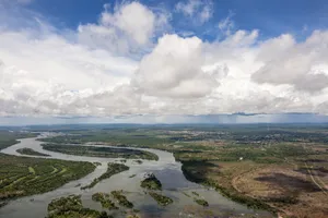 Aerial view of the Zambezi River winding through green and brown landscape in Zambia, Africa, with scattered clouds and distant horizon.