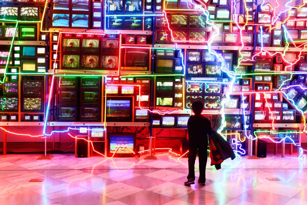 About - Hero - Nam June Paik A small child stands in front of Nam June Paik's Electronic Superhighway