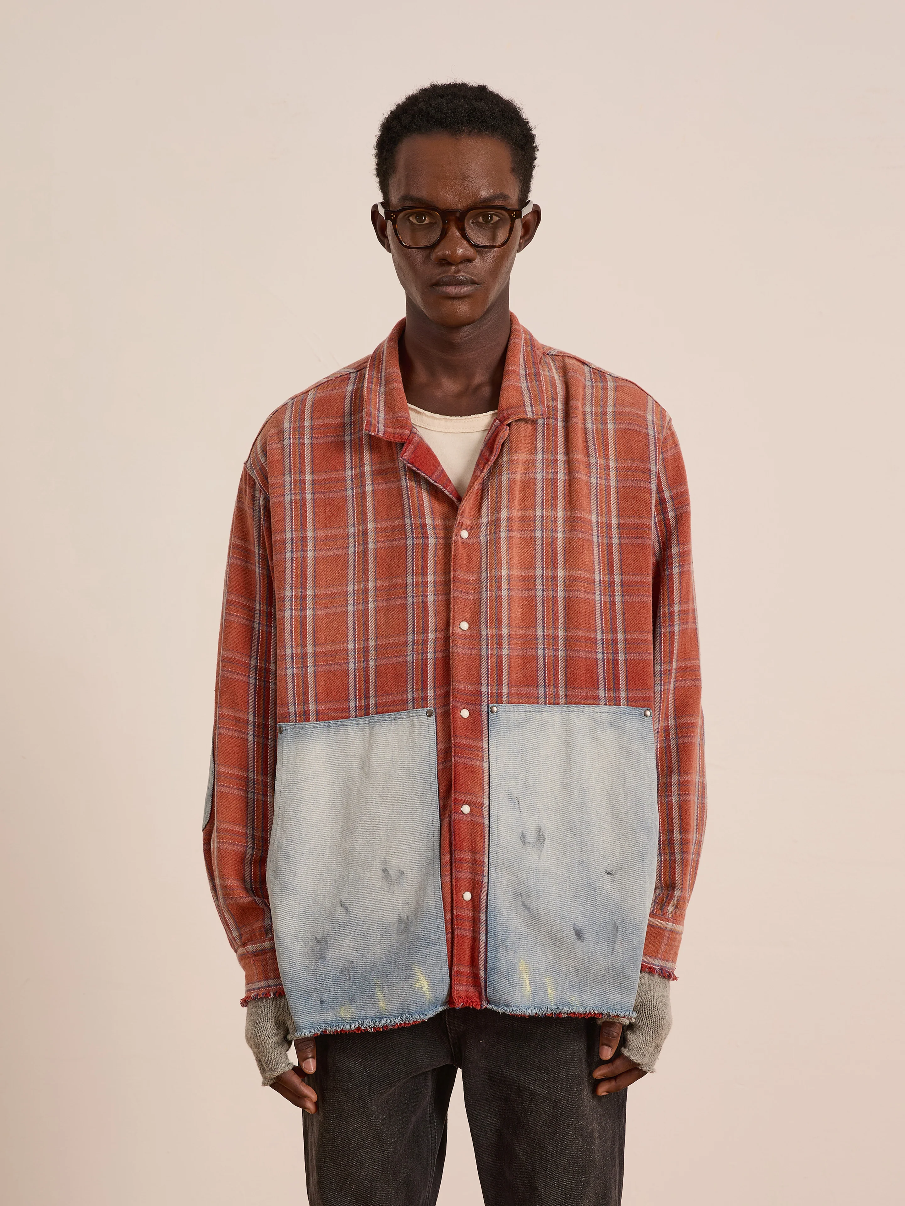 A person wearing glasses, the FOUND Plaid Denim Shirt with large denim patch pockets, fingerless gloves, and black pants stands against a plain background.