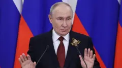 Putin resmi giysili konuşma yapıyor iki eli havada.