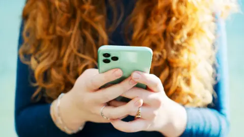 Woman with long red curly hair holds a mobile phone