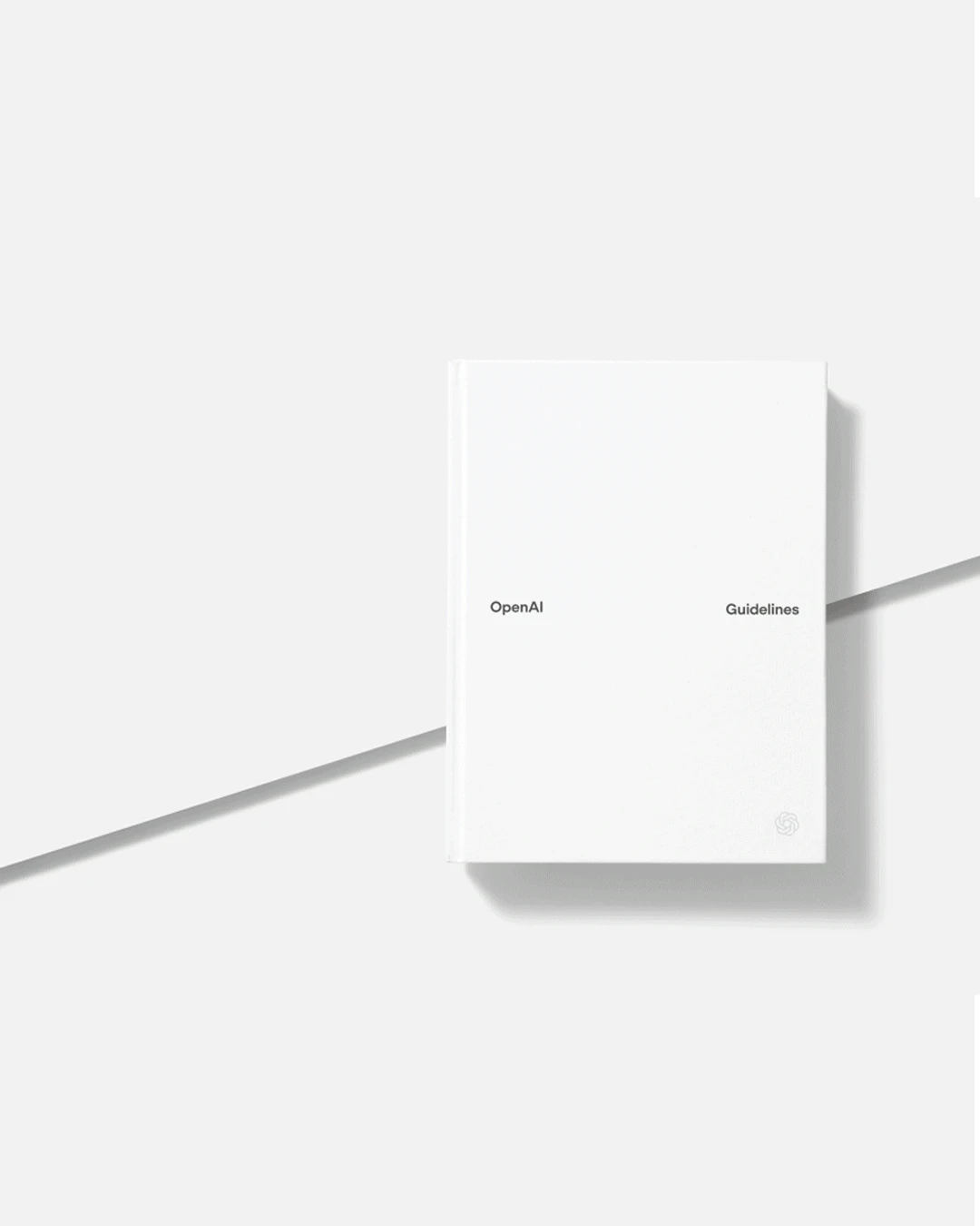 A white hardcover book titled “OpenAI Guidelines” with minimalistic text. The book lies on a light gray surface, styled with clean, geometric shadows.