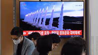 Ihmiset istuvat odotustilassa televisioruudun edessä; ruudulla näkyy ohjuksia ja koreankielistä tekstiä.