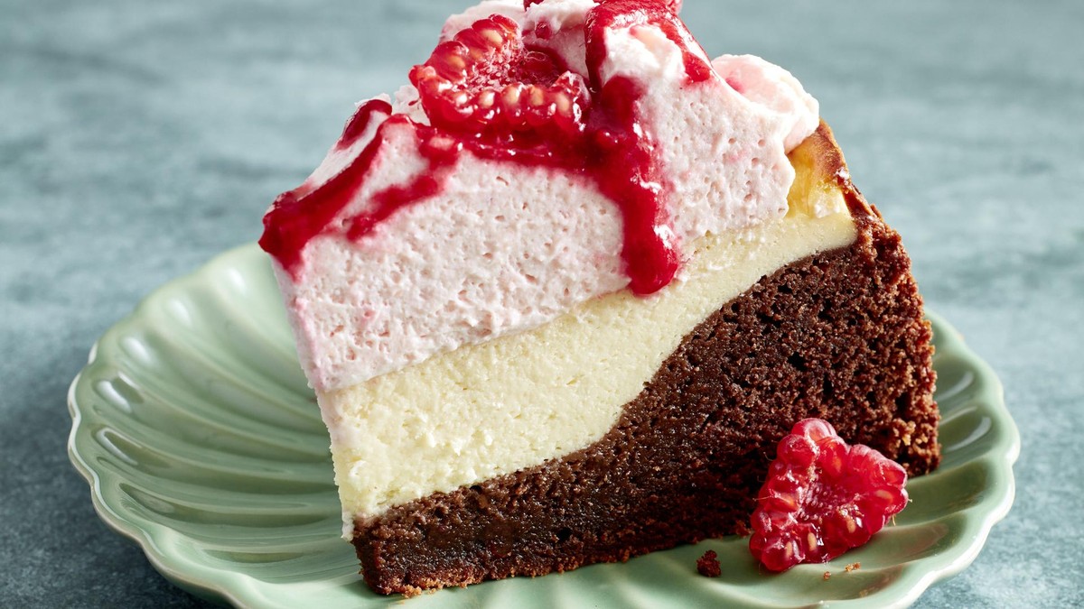 Unten schokoladig, in der Mitte cremig, oben fruchtig – hier muss sich wirklich niemand entscheiden. Ein Stück Brownie-Cheesecake mit Himbeeren
