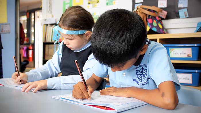 Image of two kindergarten students at their desks practising handingwriting skills.