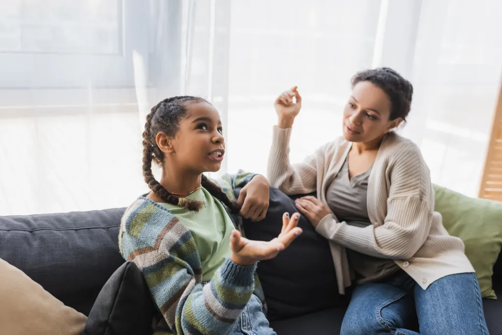 An African American teenage girl points with her hand while talking with her mother on a sofa at home on Monday, October 25, 2021.
