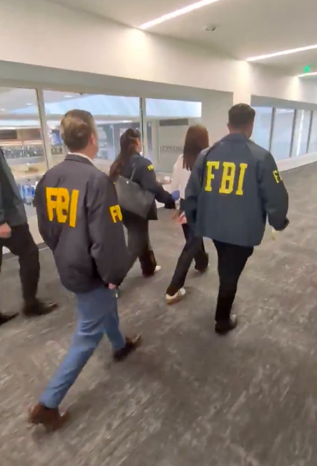 Two FBI agents escorting an individual down a hallway.