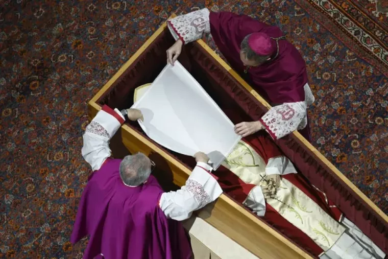 Before the wooden coffin is closed, Pope Benedict XVI’s personal secretary Archbishop Georg Gänswein and Monsignor Diego Giovanni Ravelli, the Vatican’s lead master of ceremonies for papal liturgies, place a white veil over the late pope’s face. The action on Jan. 4, 2023, is part of the funeral rites for popes. (Photo: Vatican Media / VM)