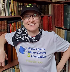 Woman with Pierce County Library Foundation shirt smiles in front of a bookshelf