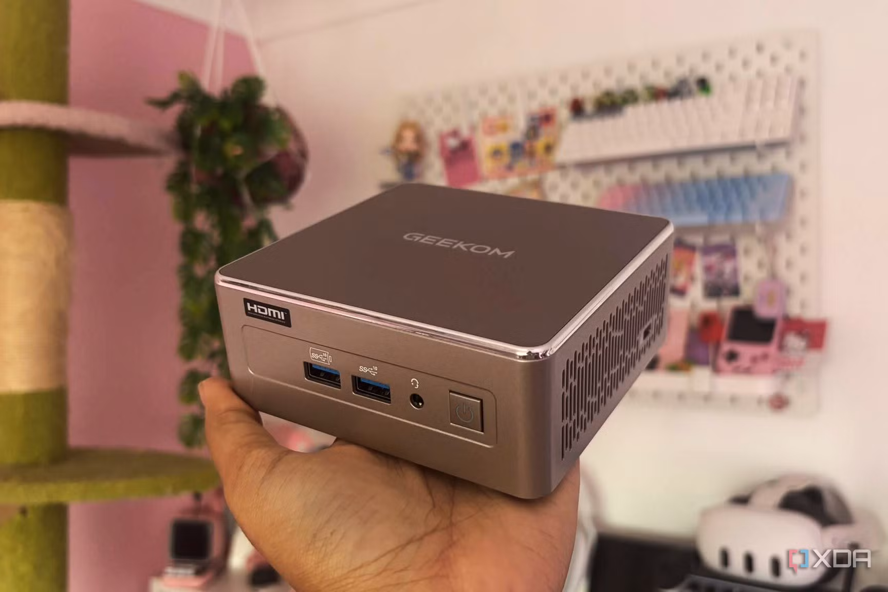 A grey mini PC in a hand with other gadgets in the background