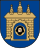 A coat of arms depicting a grey castle with three towers topped by crosses with a human head on the front door all on a blue background