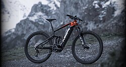 An orange and black bike sits on a misty mountain in what is probably a promotional photo. No one is on the bike and it looks relatively new.