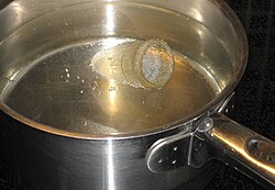 picture of a bell-shaped menstrual cup, covered in simmering water in a stainless cooking pot on a hob
