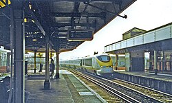A grainy photo of a Eurostar train passing through a station between two platforms with the camera on the opposite side, and the cameraperson sheltered by a canopy; the train has barely entered the platform when the photo was taken