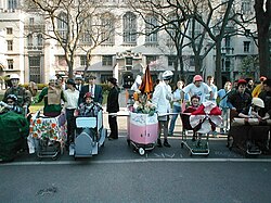 A group of students in front of six shopping carts that have been decorated; there is a student wearing a helmet in each one