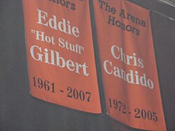 Deux bannières orange suspendu au plafond d'une salle. Sur celle de gauche est écrit Eddie Gilbert et sur la seconde Chris Candido.