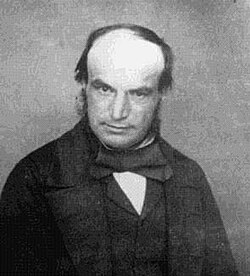 Photo en noir et blanc de John Couch Adams, le crâne très dégarni et vêtu d'un costume.