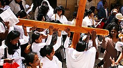 A group of Christian women wearing white walking with a horizontal cross in a crowd