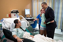Photo of Obama smiling at a hospital patient while hugging her friend