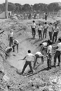A dozen men digging a deep hole