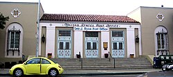 The entrance of a post office. There are several cars in front of it.