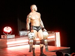 Randy Orton en slip entrant sur le ring avec une ceinture dans chaque main.