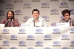 Three men sit at a table at a convention.