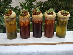 Five shot glasses of different coloured sauces, with a panipuri placed atop each.