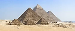 Foto Piramida Giza dengan tiga piramida utama di tengah, berlatar langit biru
