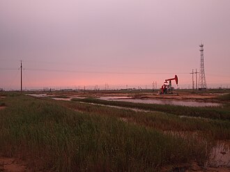 An oil well in the distance with grass and wetlands in the foreground