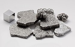 Minério acinzentado, chamado ferro, em cubo e em pedaços separados.