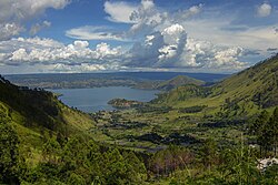 Blue waters of Lake Toba winding between steep green hills viewed from above.