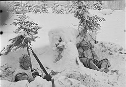 Photo noir et blanc de deux hommes en tenue blanche, allongés dans la neige, dont l'un est visiblement frigorifié.