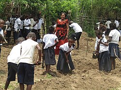 A group of children in school uniforms holding agriculture tools.