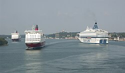Baai; links bebost en rechts bebouwing; links varen twee grote cruiseschepen naar de kijker toe en rechts vaart er eentje van de kijker af