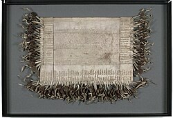 A weathered piece of parchment 20 inches long and 30 1/2 inches wide with faded Latin text in the centre and a 100 signatures around the sides with corresponding wax seals attached.