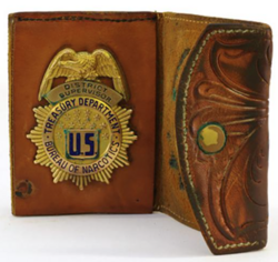 old leather wallet unfolded, dusty from sitting in a museum. Inside the fold is the badge of the Federal Bureau Of Narcotics
