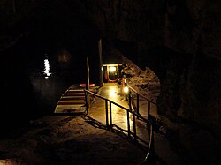 A boat moored beside a concrete path on an underground lake, with darkness surrounding.