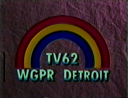 On a dark purple textured background, a rainbow consisting of three colors—blue, yellow, and red, from inside to outside. Beneath the rainbow is the text "TV62 / WGPR DETROIT" in a light green.