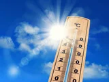 Hitze Thermometer, das 38°C anzeigt vor blauem Himmel und gleißend heller Sonne
