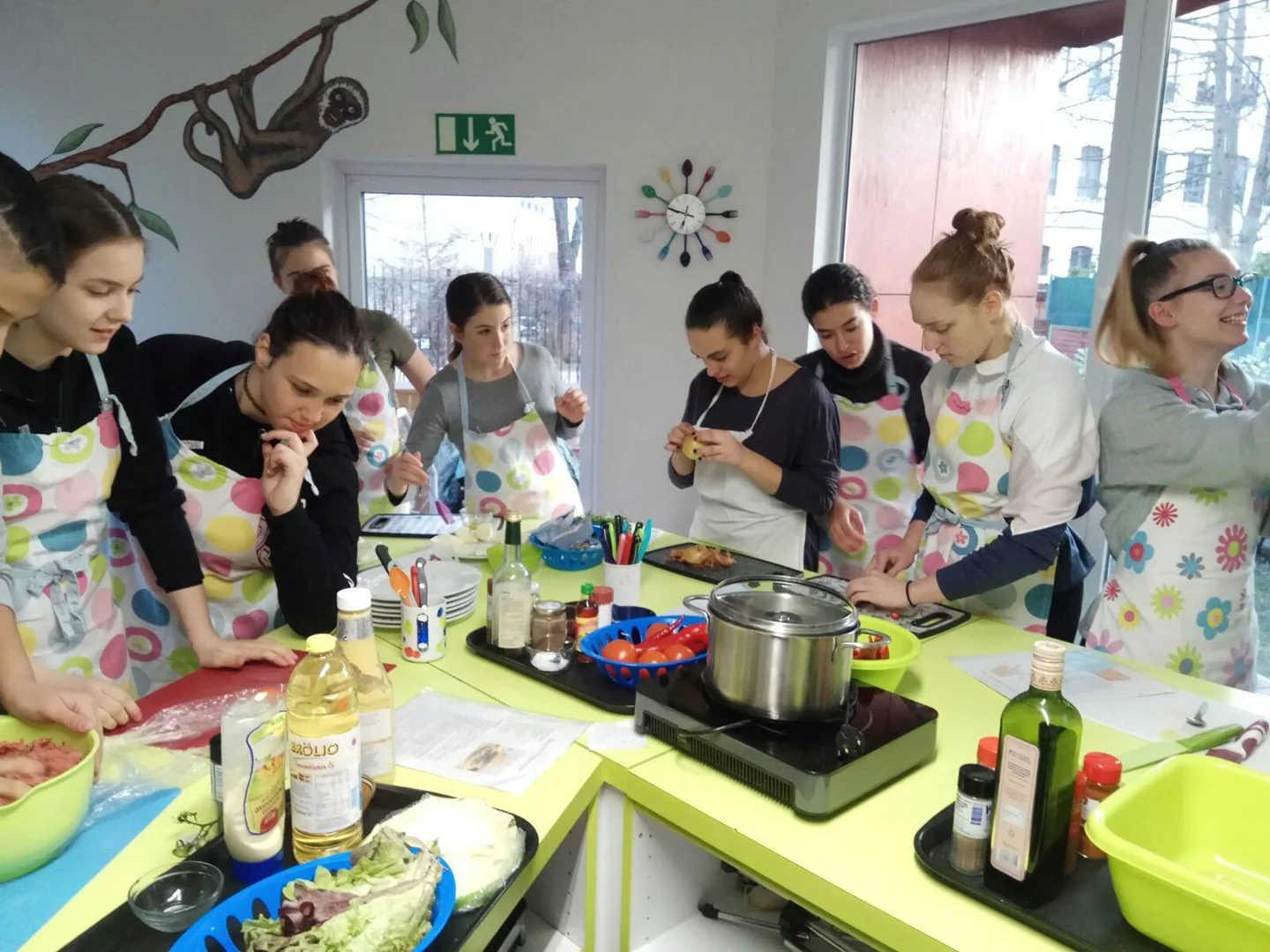 2018 Handballerinnen aus Leipzig und Herzliya kochen gemeinsam Jugendliche kochen gemeinsam, tragen bunte Schürzen, lesen an hellgrünen Arbeitsplatten Kochrezepte und scherzen