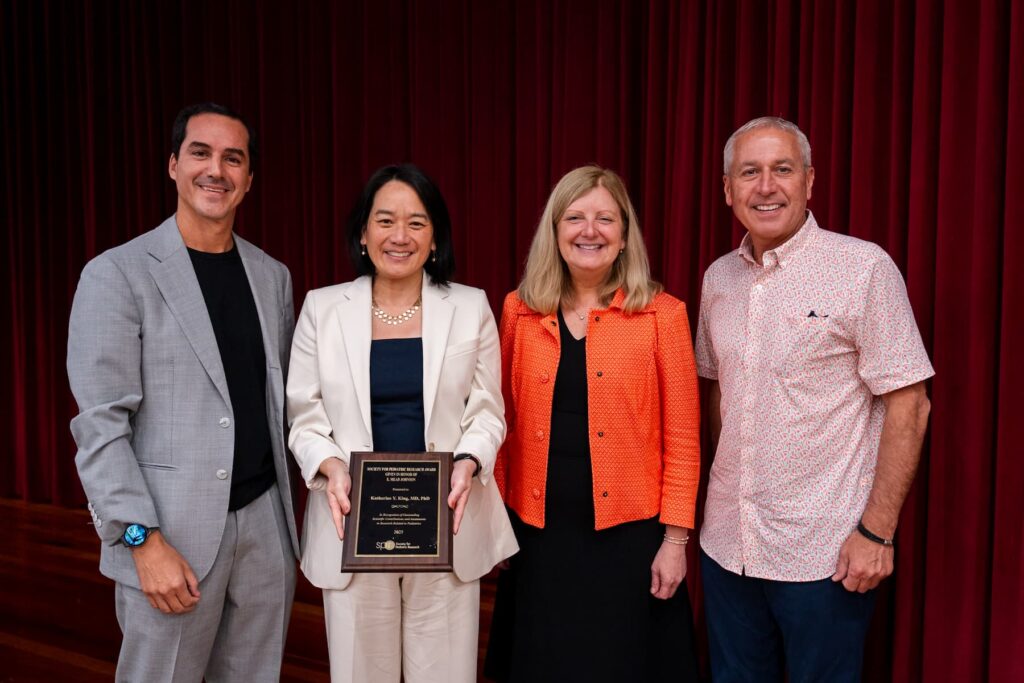 Four people standing in front of a red curtain, with one person holding a plaque.